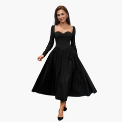 Model draagt een zwarte AKILA™ maxi-jurk met hartvormige halslijn en lange mouwen in een elegante setting.