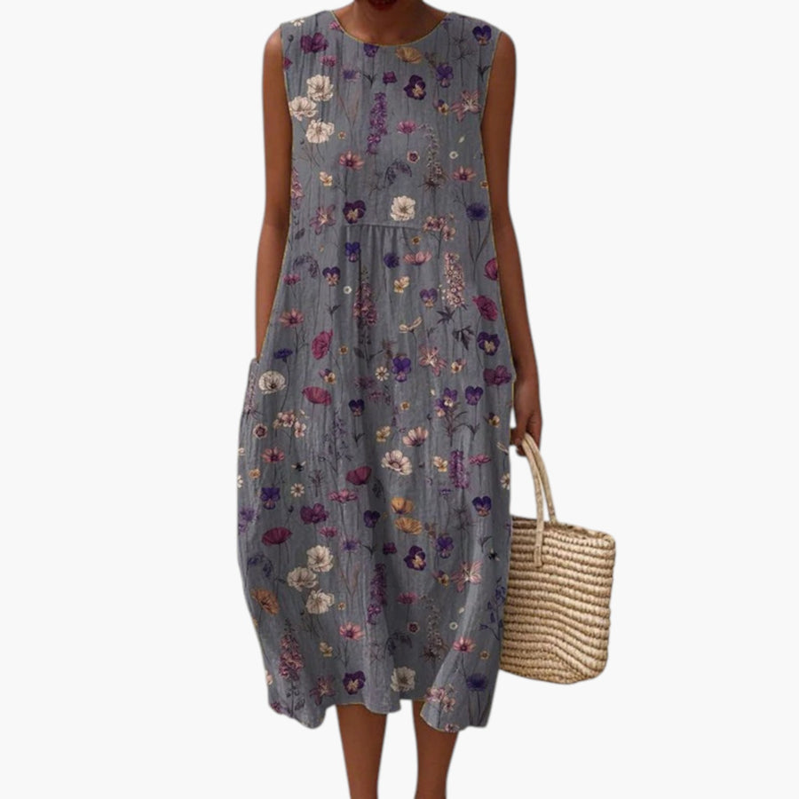 My Store 4 Gwen midi jurk met grijs bloemenpatroon in paars, ivoor en goud op het strand met een rieten tas