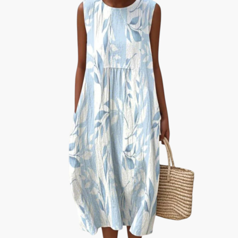 My Store 4 Joy™ Leafy midi-jurk met blauw-witte bladerenprint, mouwloos model op het strand met rieten tas.