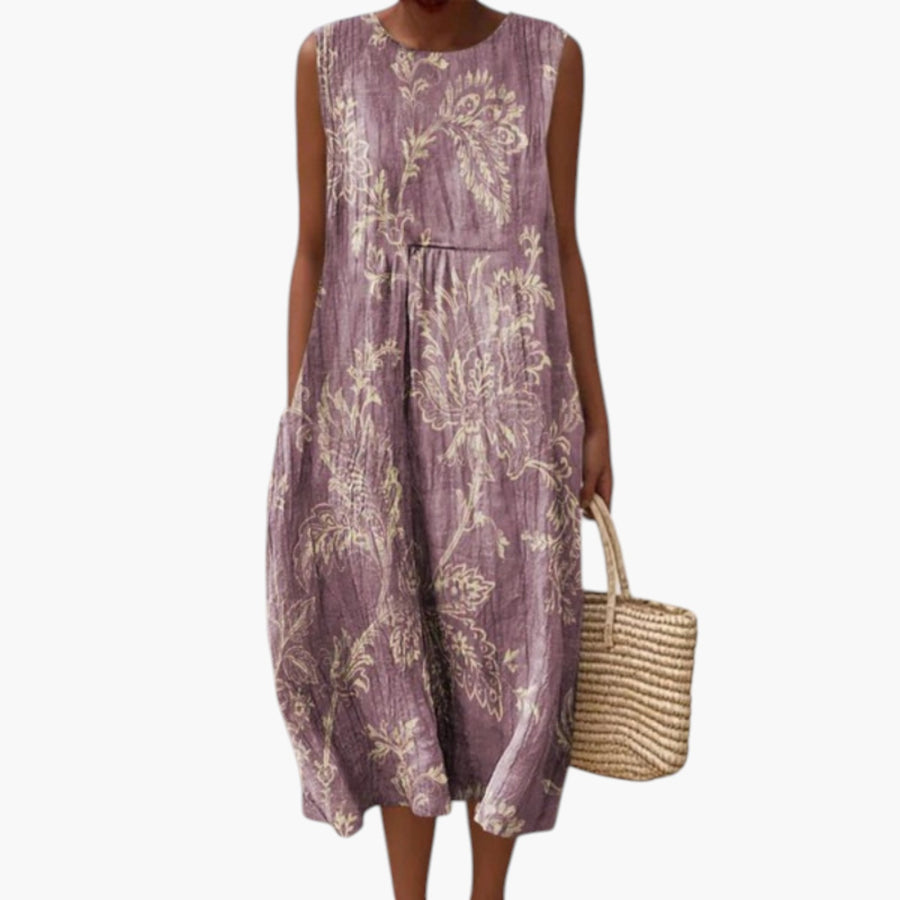 My Store 4 Mia midi jurk in paars met crèmekleurige bloemenprint, mouwloos model op het strand met rieten tas.