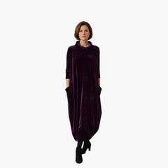 Vrouw draagt een paarse My Store 4 Leona fluwelen maxi-jurk met opstaande kraag en zakken in een minimalistisch interieur