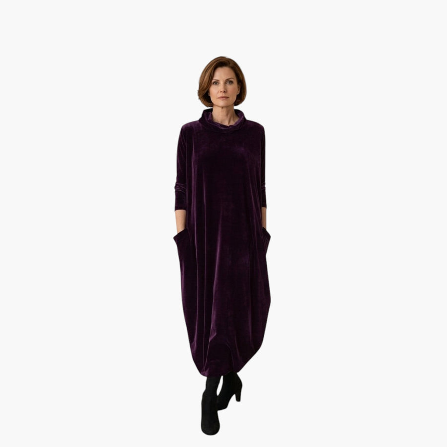 Vrouw draagt een paarse My Store 4 Leona fluwelen maxi-jurk met opstaande kraag en zakken in een minimalistisch interieur