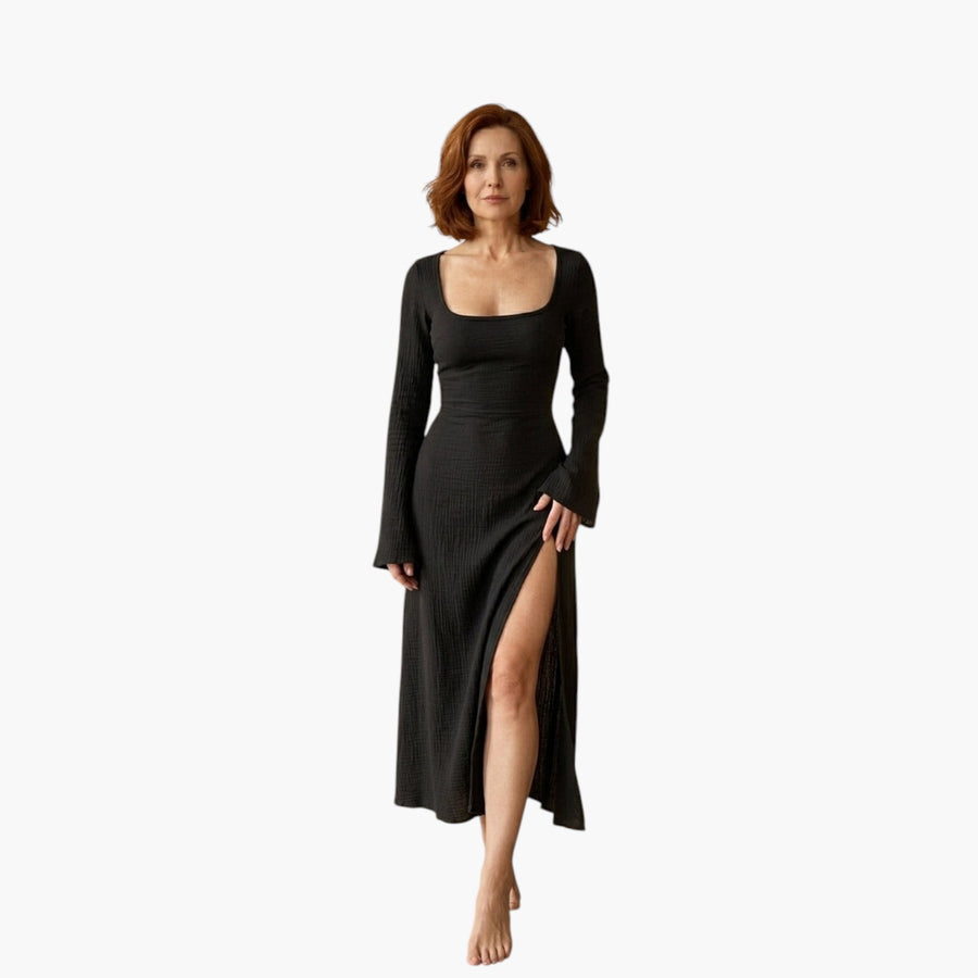 Vrouw draagt een elegante zwarte TILA™ jurk met flounce mouwen, vierkante halslijn en hoge split in een lichte studio.